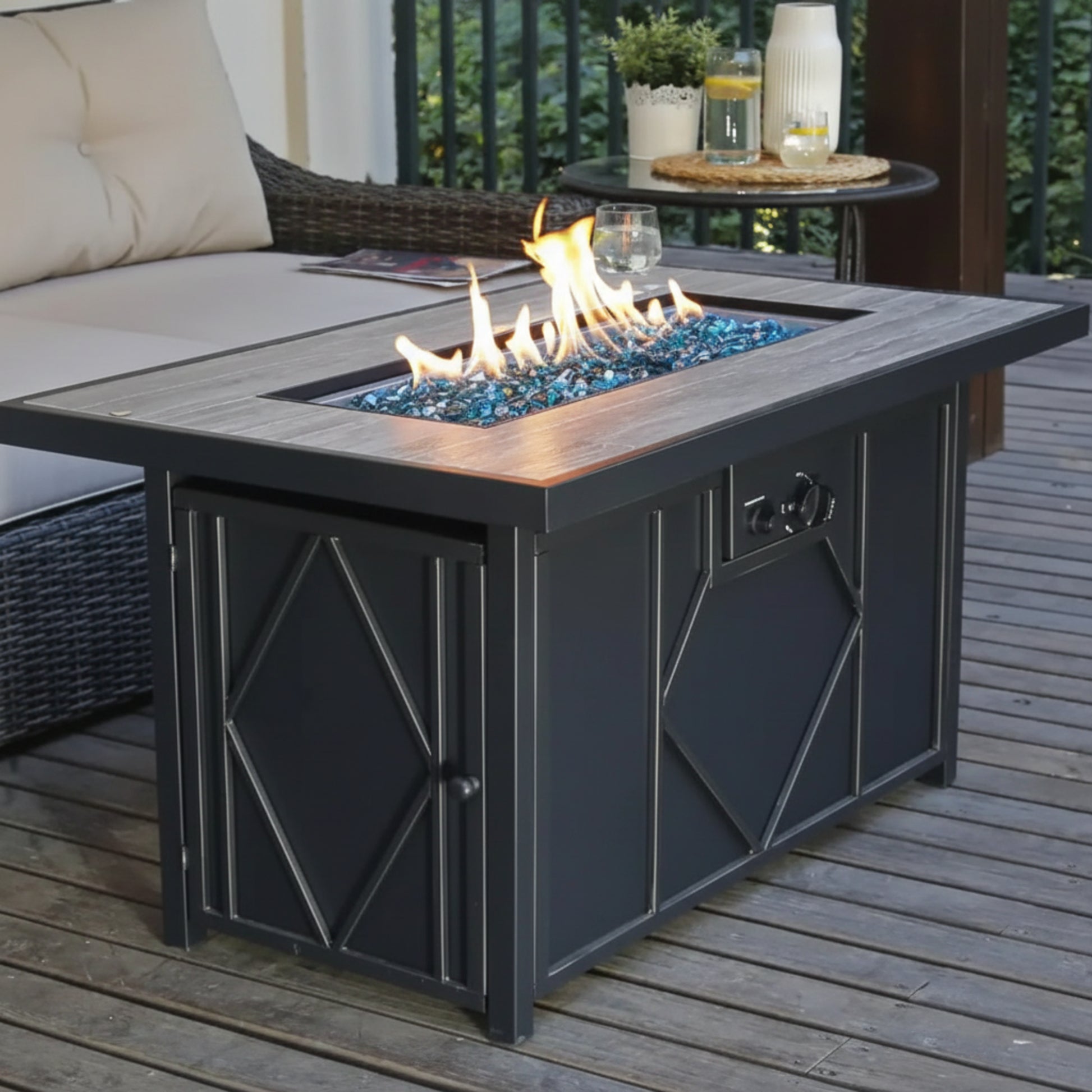 Outdoor fire pit table with flames on a wooden deck, surrounded by patio furniture.
